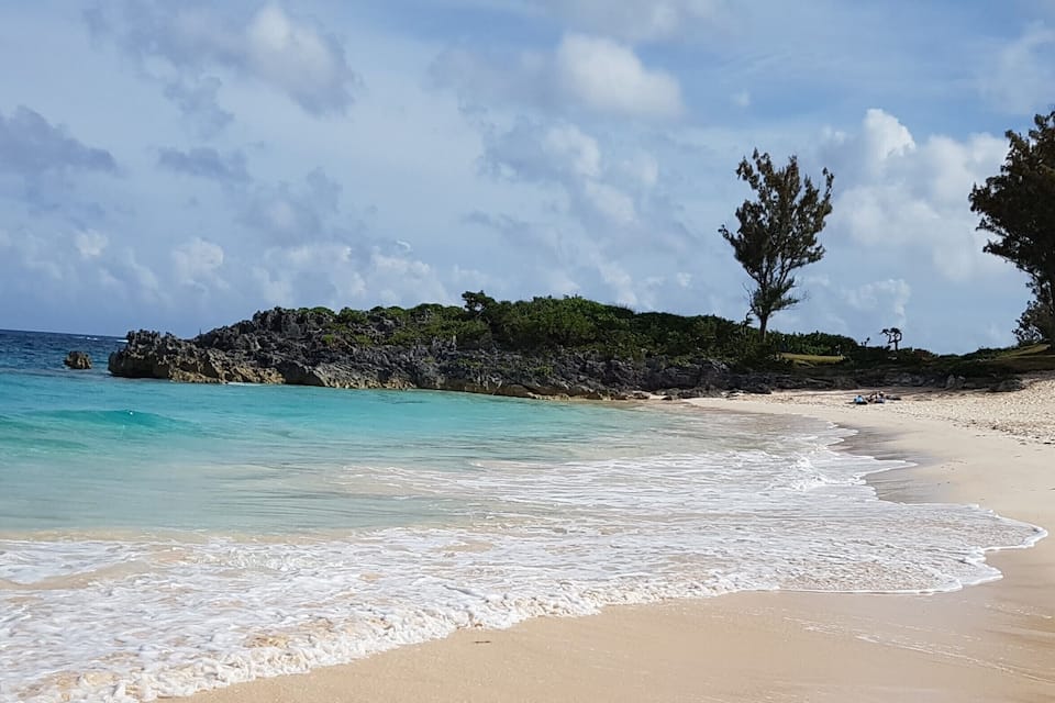 A beach with clear turquoise water, sandy shore, and rocky outcrops with vegetation.