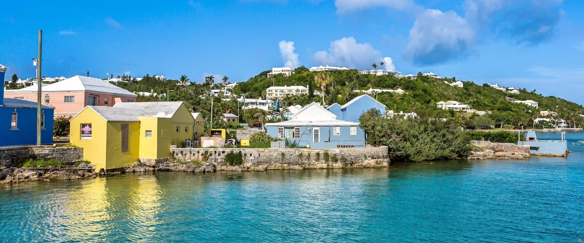 A coastal town with colorful buildings by the water, a hill with houses, and a clear blue sky.