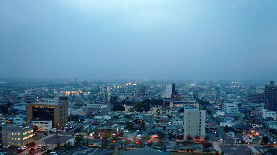 A cityscape at dusk with buildings, roads, and a parking lot.