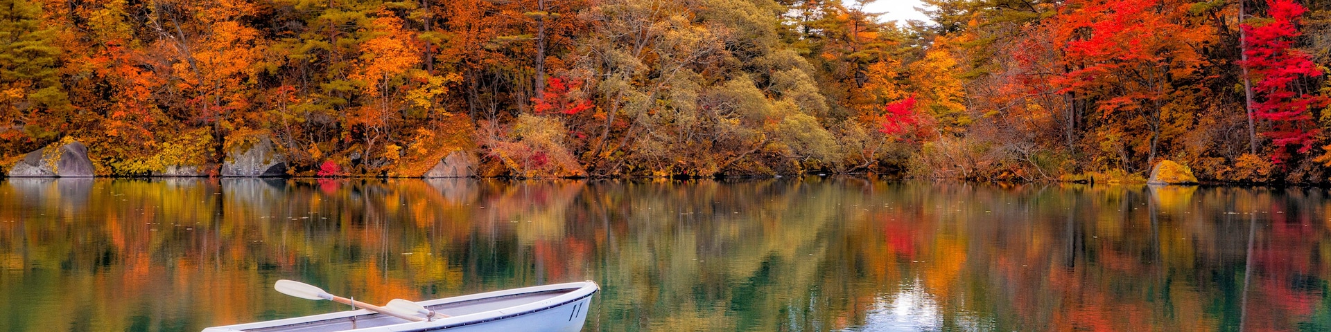 Um lago tranquilo com um barco a remos, rodeado por árvores com folhagem outonal.
