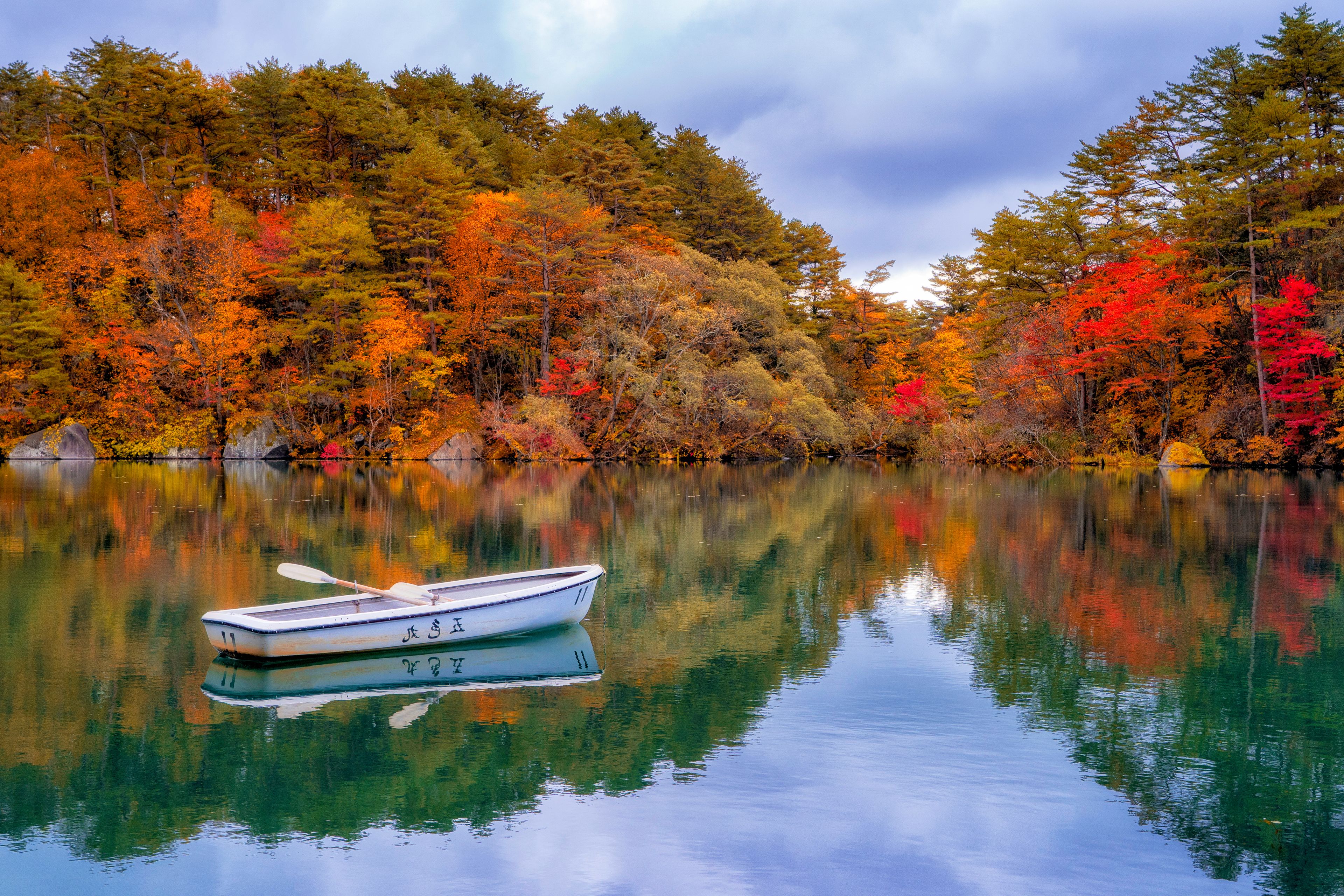 A calm lake with a rowboat, surrounded by autumn-colored trees.