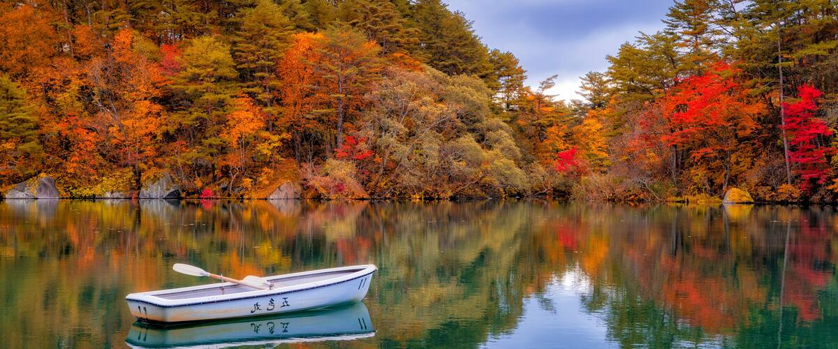 A calm lake with a rowboat, surrounded by autumn-colored trees.