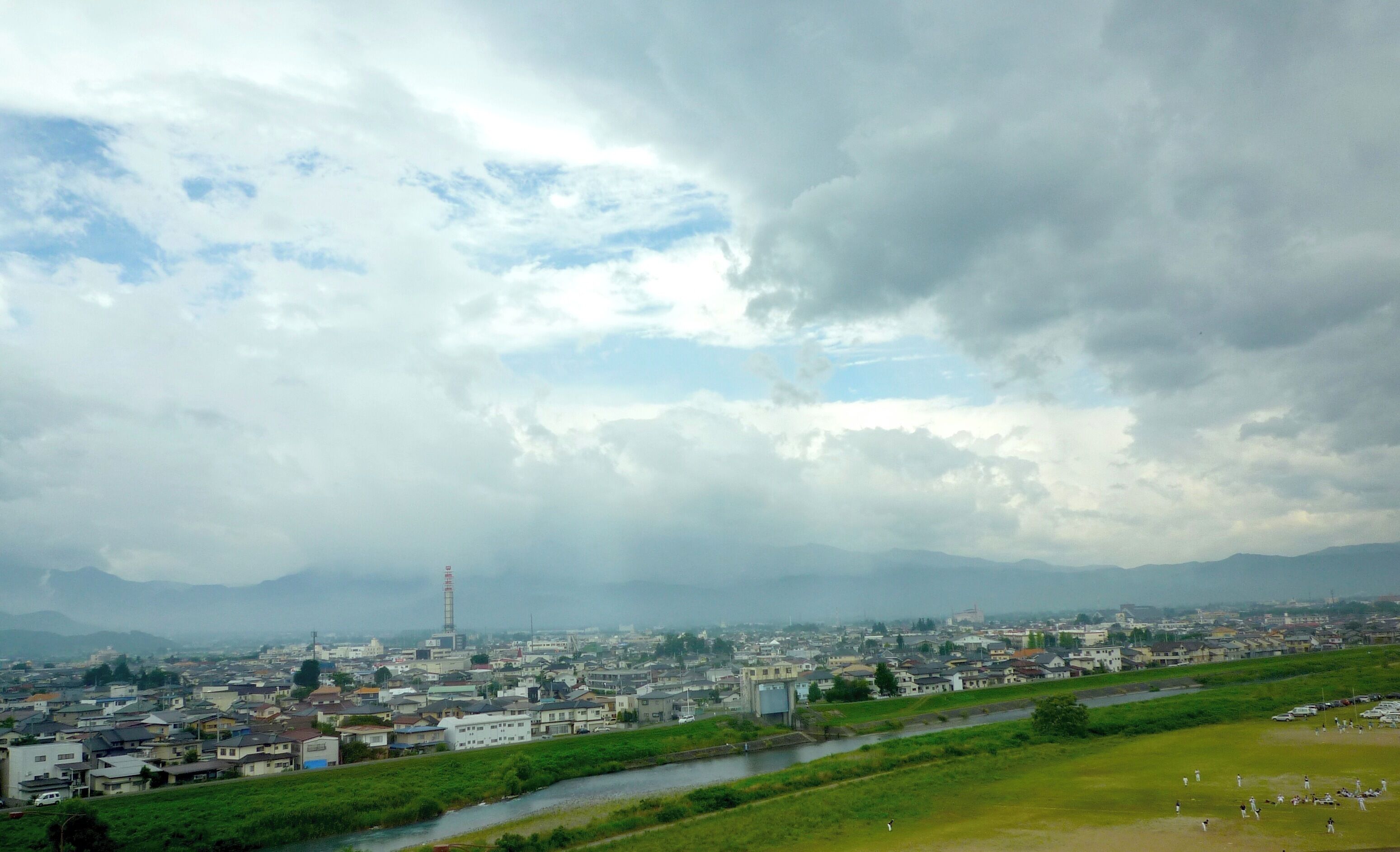 A cityscape with a river, green fields, and mountains in the background.