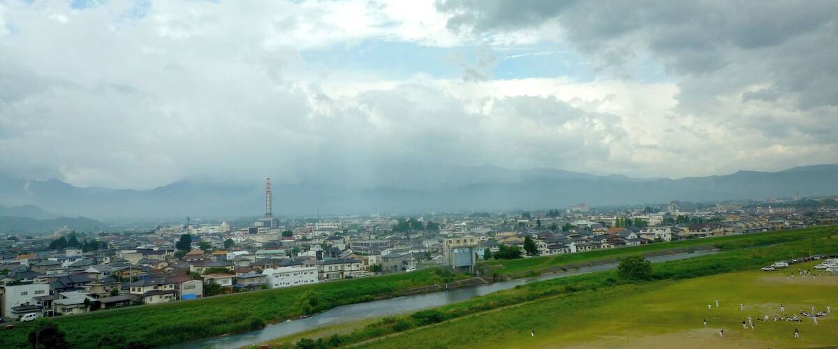 A cityscape with a river, green fields, and mountains in the background.