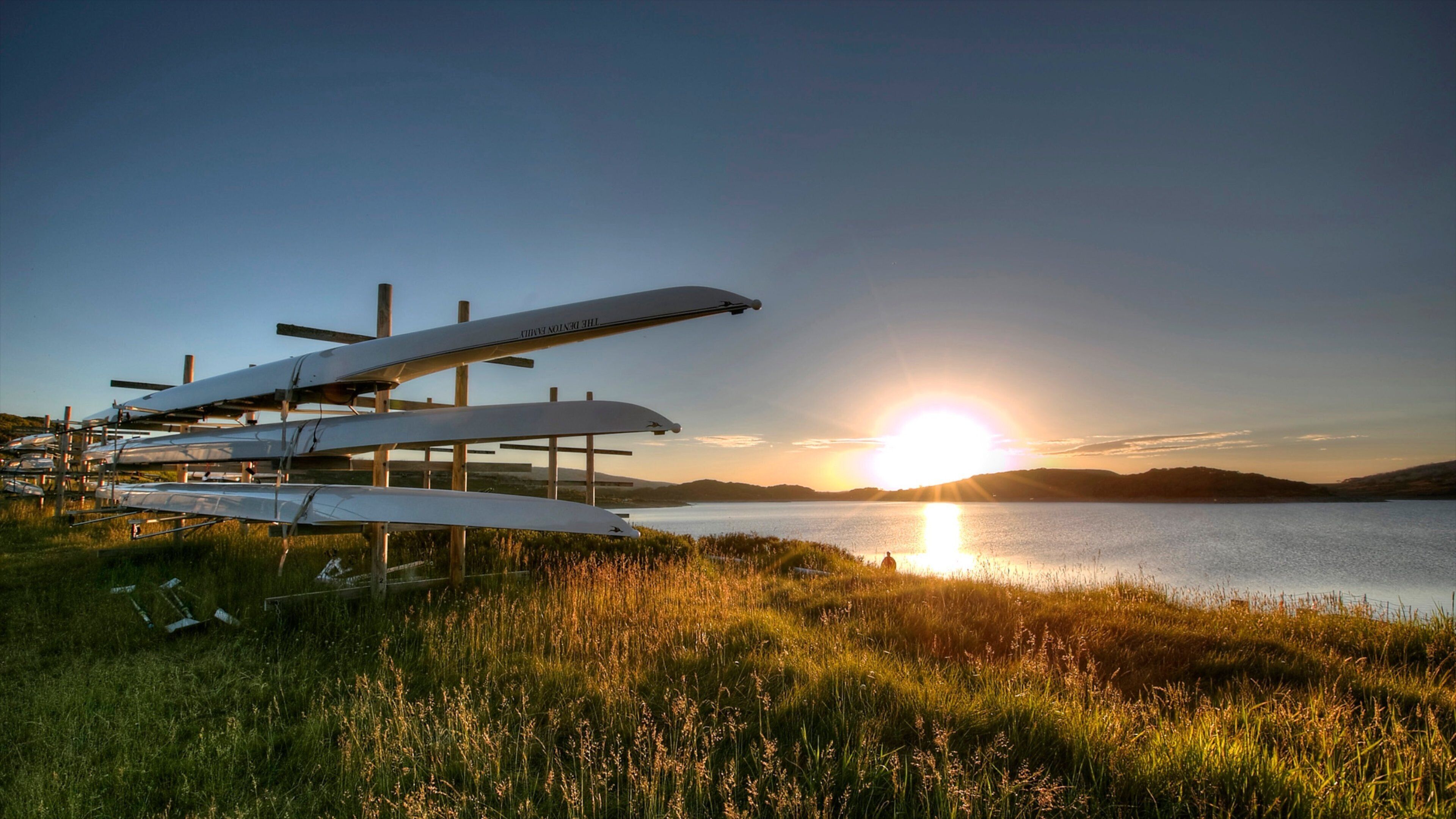 A sunset over a lake with several sailplanes parked on a grassy field.