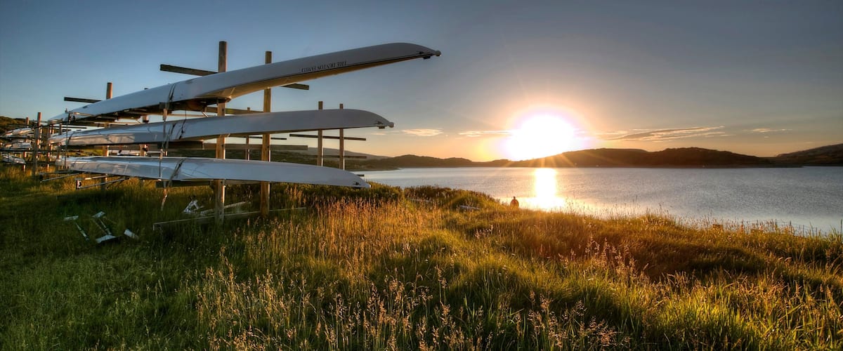 A sunset over a lake with several sailplanes parked on a grassy field.