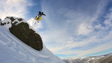A snowboarder mid-air performing a jump over a snow-covered mountain with a clear sky in the background.