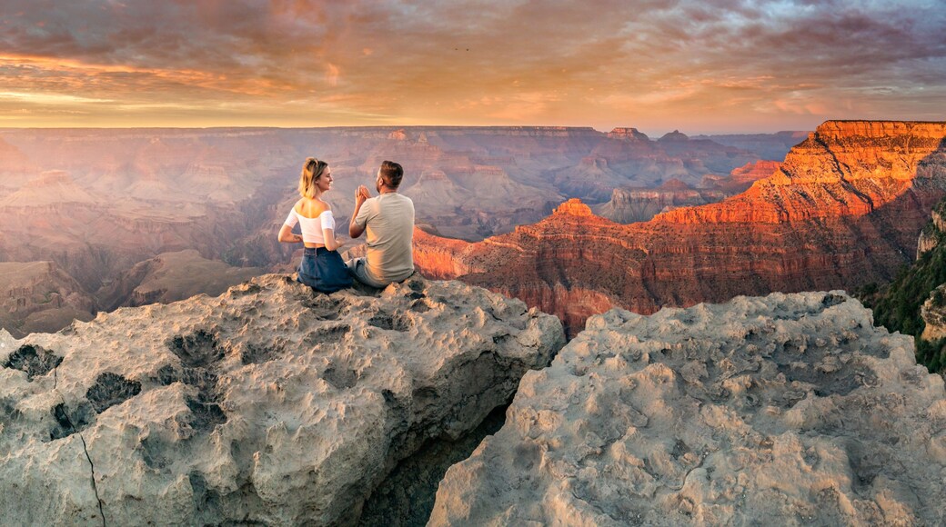 Man and woman sit on the edge of the rim having great conversation during the Grand Canyon sunset