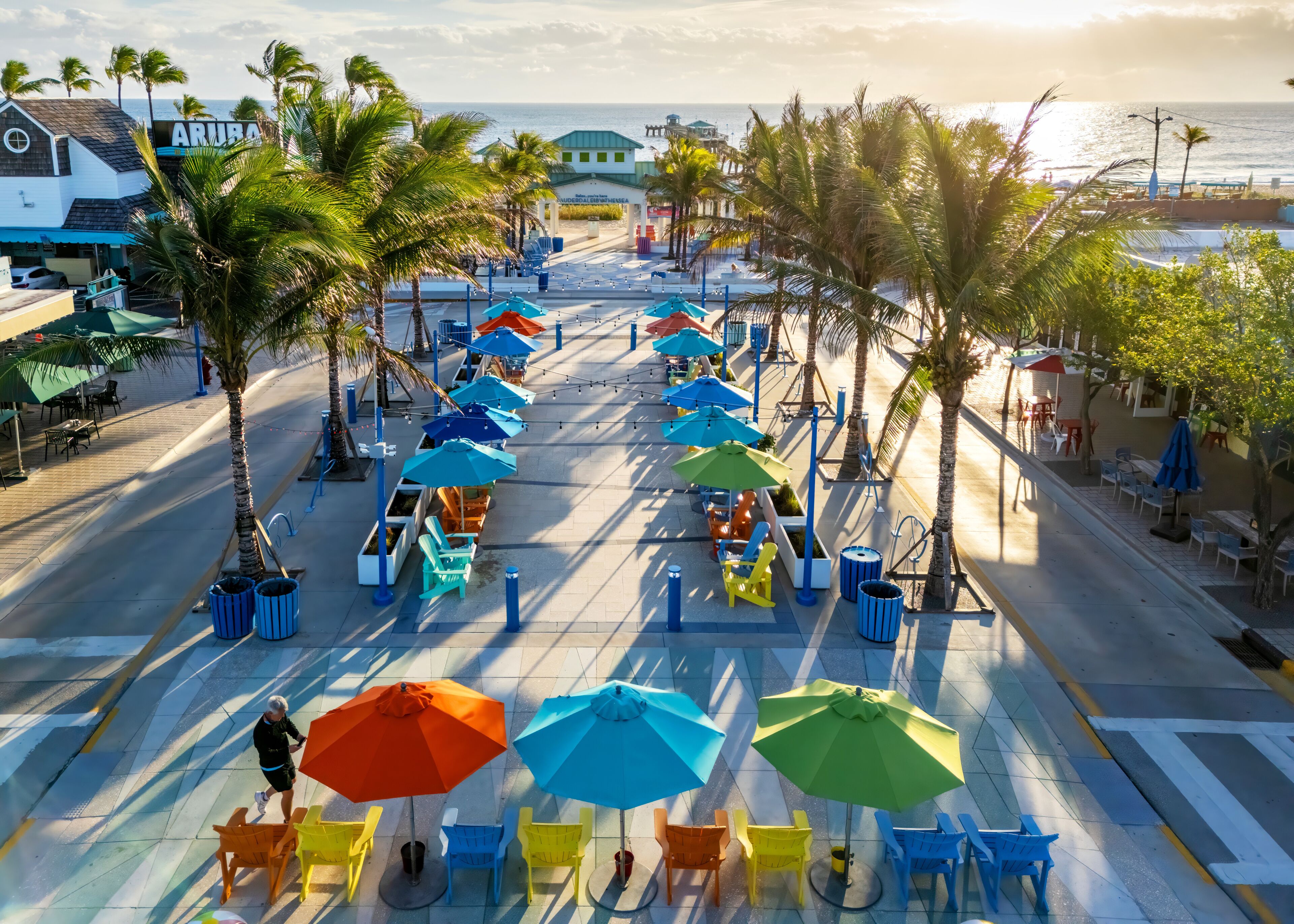 Un paseo marítimo en la playa con sombrillas coloridas, sillas y palmeras.