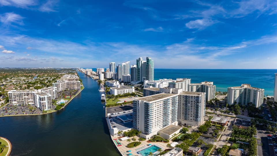 A coastal cityscape with a river, high-rise buildings, and a clear blue sky.