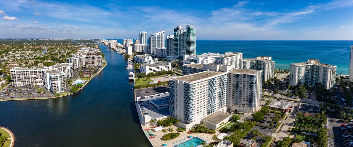 A coastal cityscape with a river, high-rise buildings, and a clear blue sky.