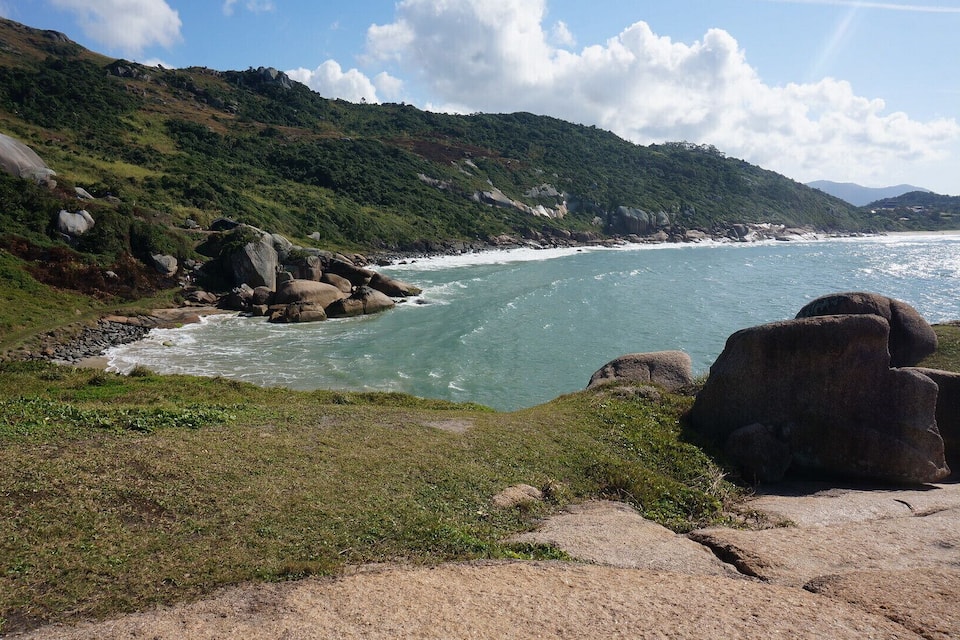 A coastal landscape with a rocky shoreline, green hills, and a clear sky.