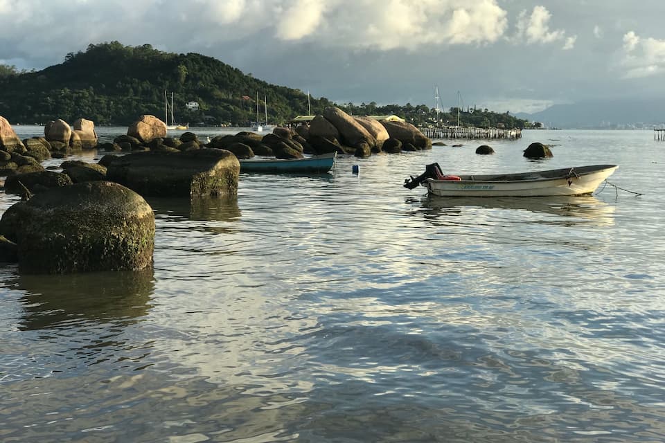 Una baia tranquilla con grandi rocce, una piccola barca e una collina lontana con una casa.