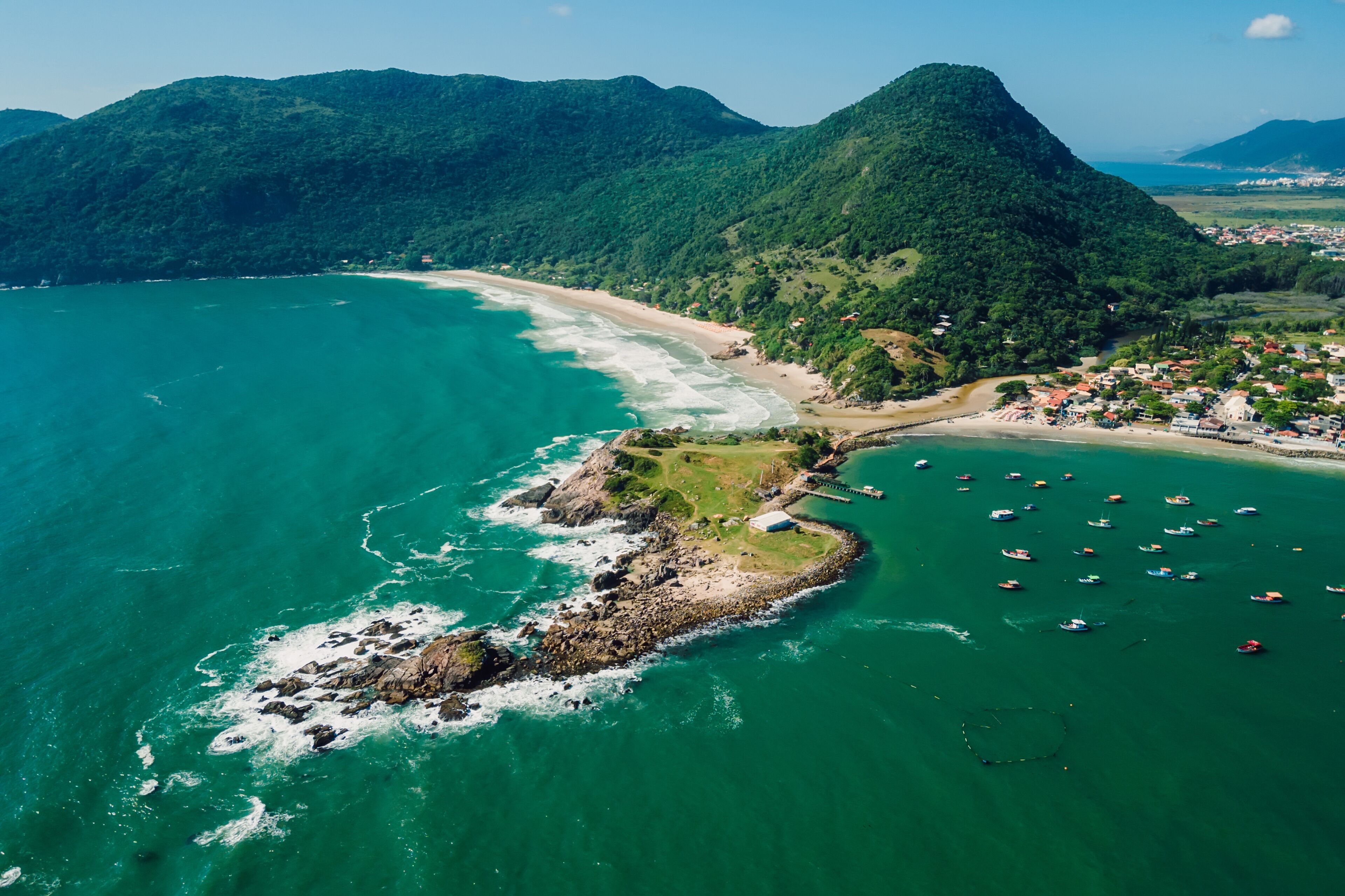 Paisagem costeira com praia, uma pequena ilha com afloramentos rochosos e uma vila com edifícios.