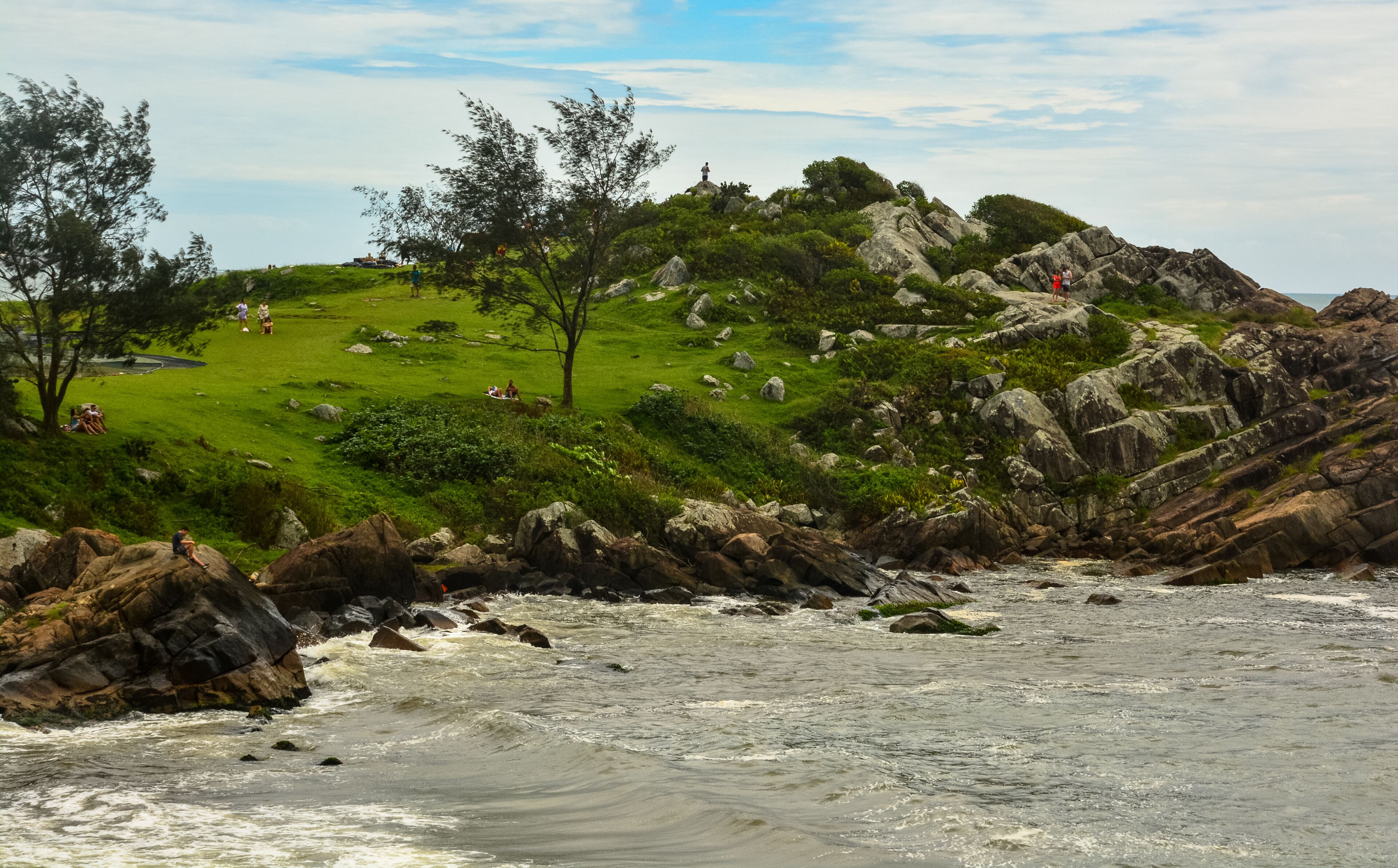 Un paisaje costero con una colina cubierta de hierba, afloramientos rocosos y un mar agitado.