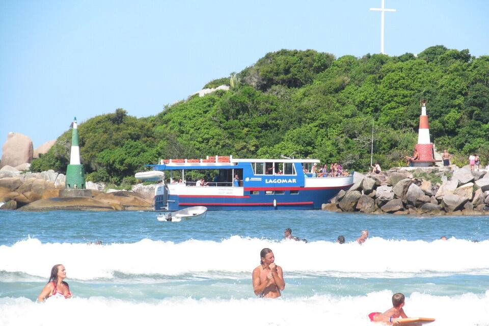 A boat named 'LAGOMAR' on calm waters, a lighthouse, and people enjoying the beach.