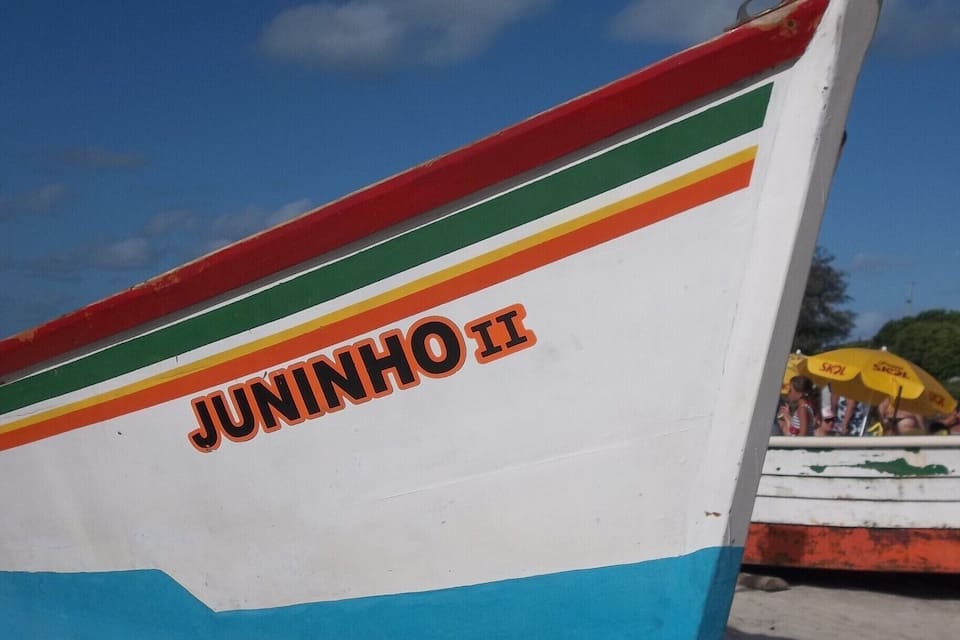 Una embarcación colorida con el nombre "JUNINHO II" en su lateral, descansando sobre una playa arenosa.