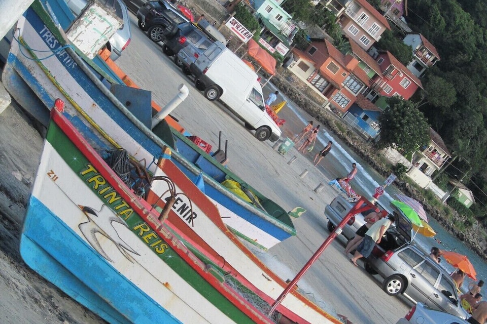 Una playa con barcos de colores, un estacionamiento y edificios al fondo.