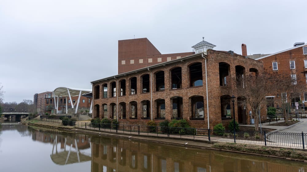 A historic brick building with arched windows and a river in the foreground.