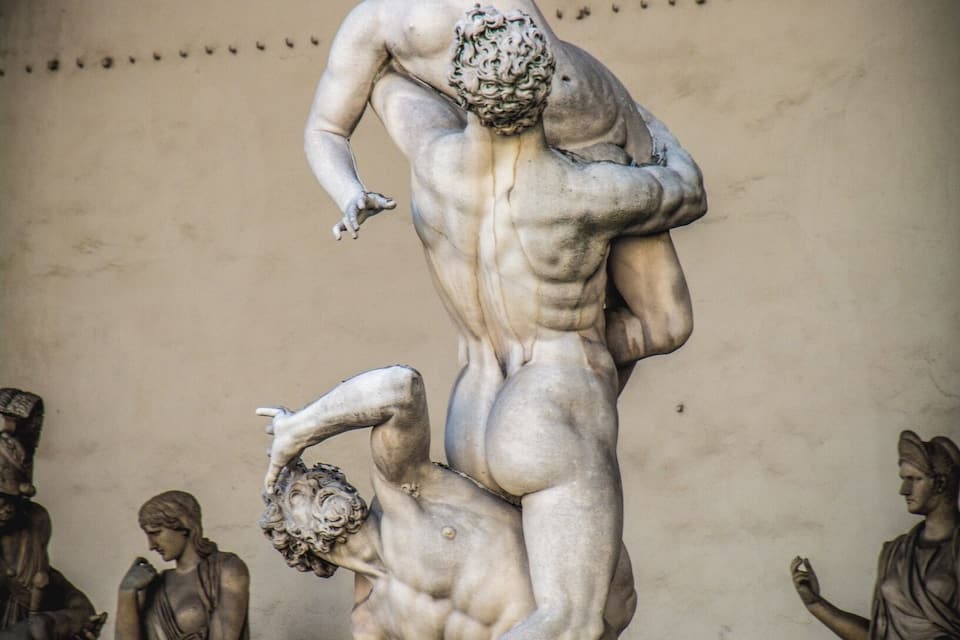 A marble sculpture of a male figure lifting another figure in a dynamic pose, surrounded by other statues.