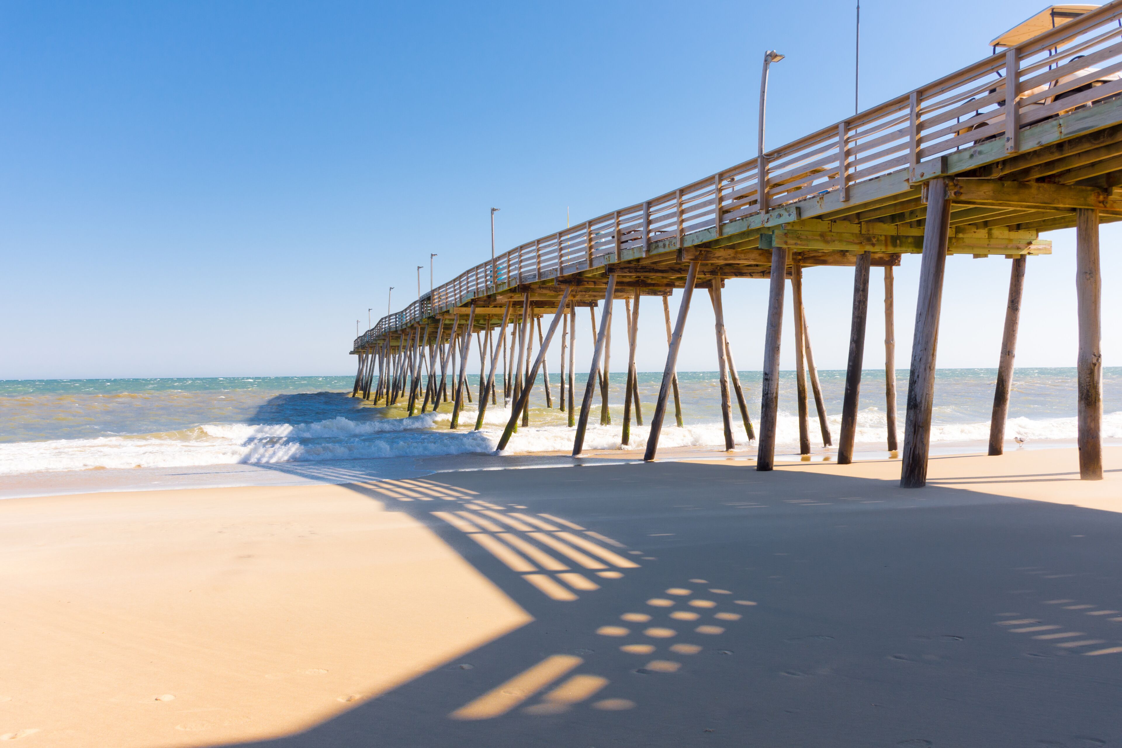 Kitty Hawk Pier in bright sunshine with shadows, ocean, and clear blue sky