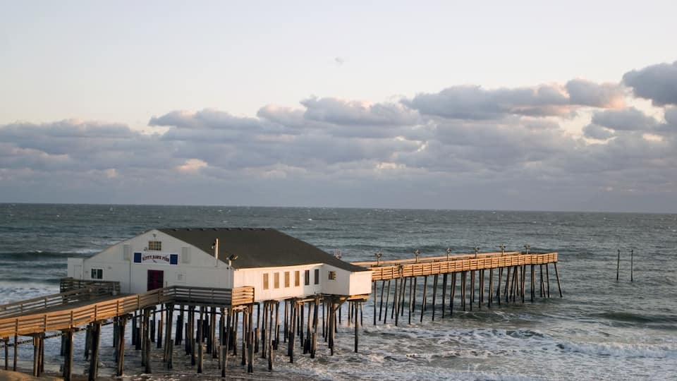 A pier with a white building at the end, wooden walkways, and the ocean.