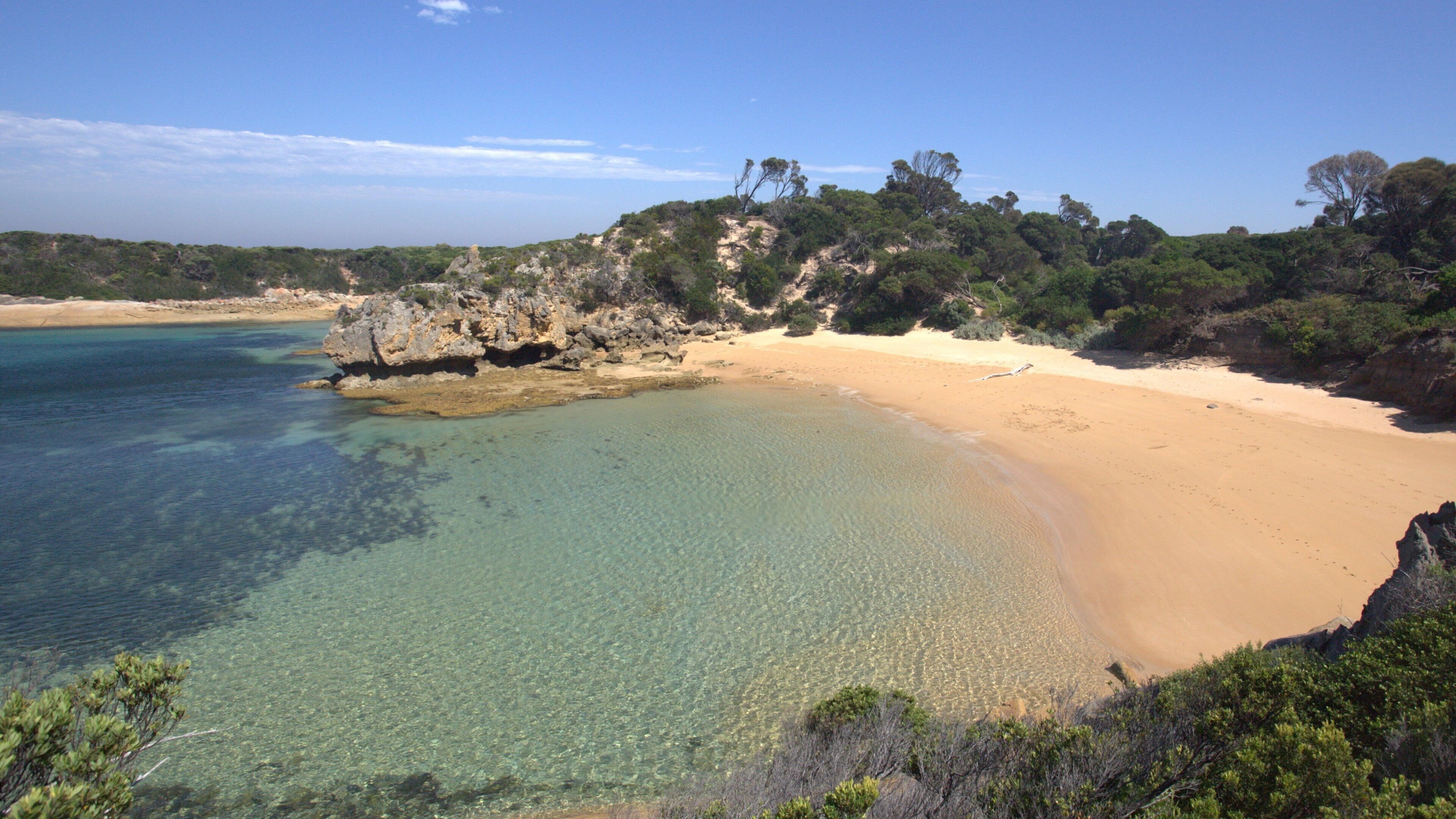 A beach with clear turquoise water, sandy shore, and rocky cliffs with sparse vegetation.