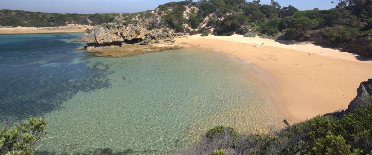 A beach with clear turquoise water, sandy shore, and rocky cliffs with sparse vegetation.