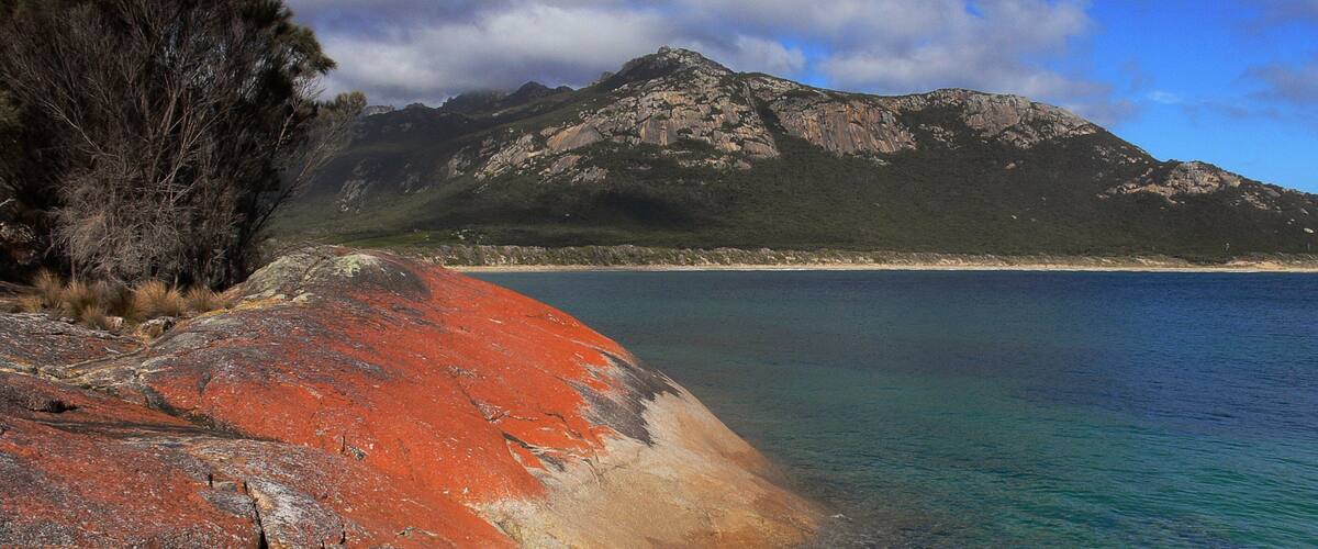 A coastal landscape with a rocky shoreline, a clear blue sea, and a mountain in the background.
