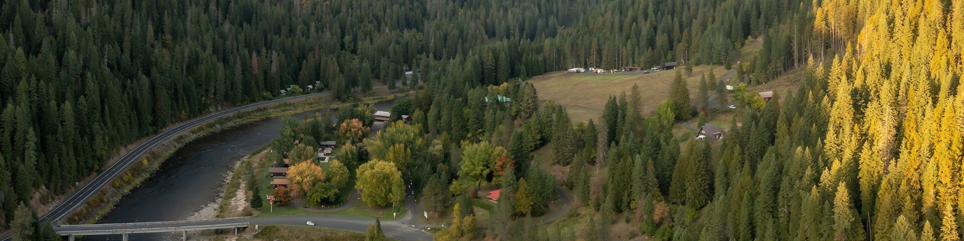 Aerial view of a river winding through a valley, surrounded by lush forests. A road and small cabins are visible along the riverbank. Nez Perce-Clearwater National Forest, Lowell, Idaho, USA.