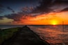 A sunset over a body of water with a stone pathway leading to the water's edge.