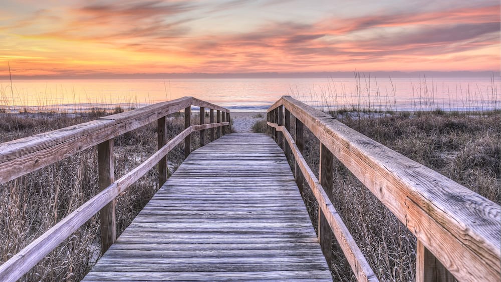 Une promenade en bois menant à une plage au coucher du soleil.
