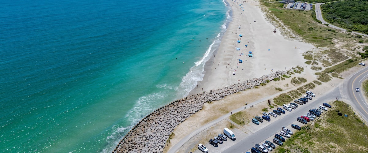 A coastal road with a beach, parked cars, and a clear blue ocean.