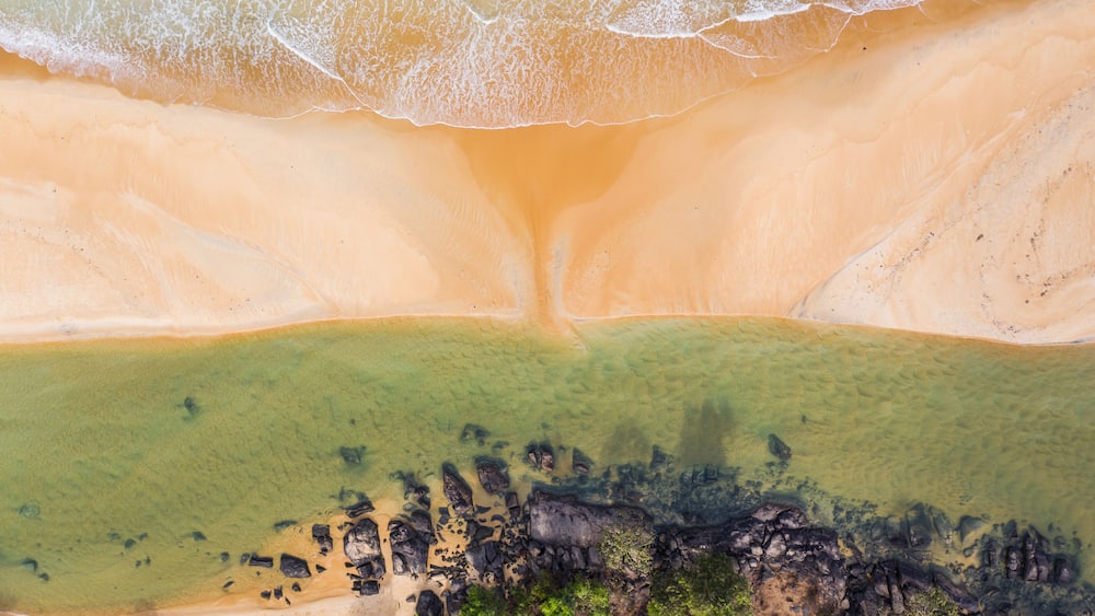 A beach with clear water, a sandy shore, and visible rocks.