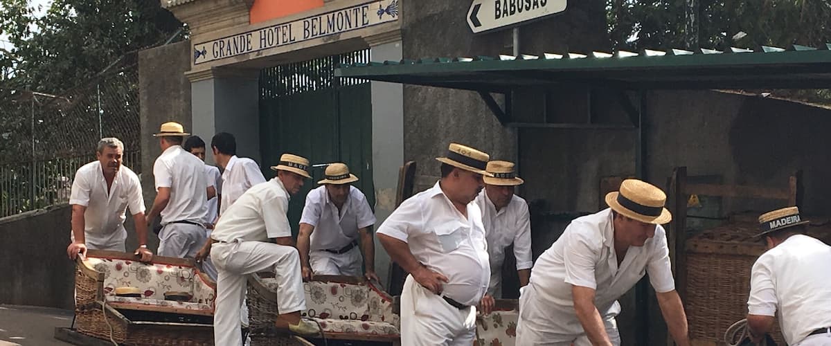 Homes amb uniforme i gorra blanca carregant mobles de vimet sobre un carret davant l'Hotel Grande Belmonte.