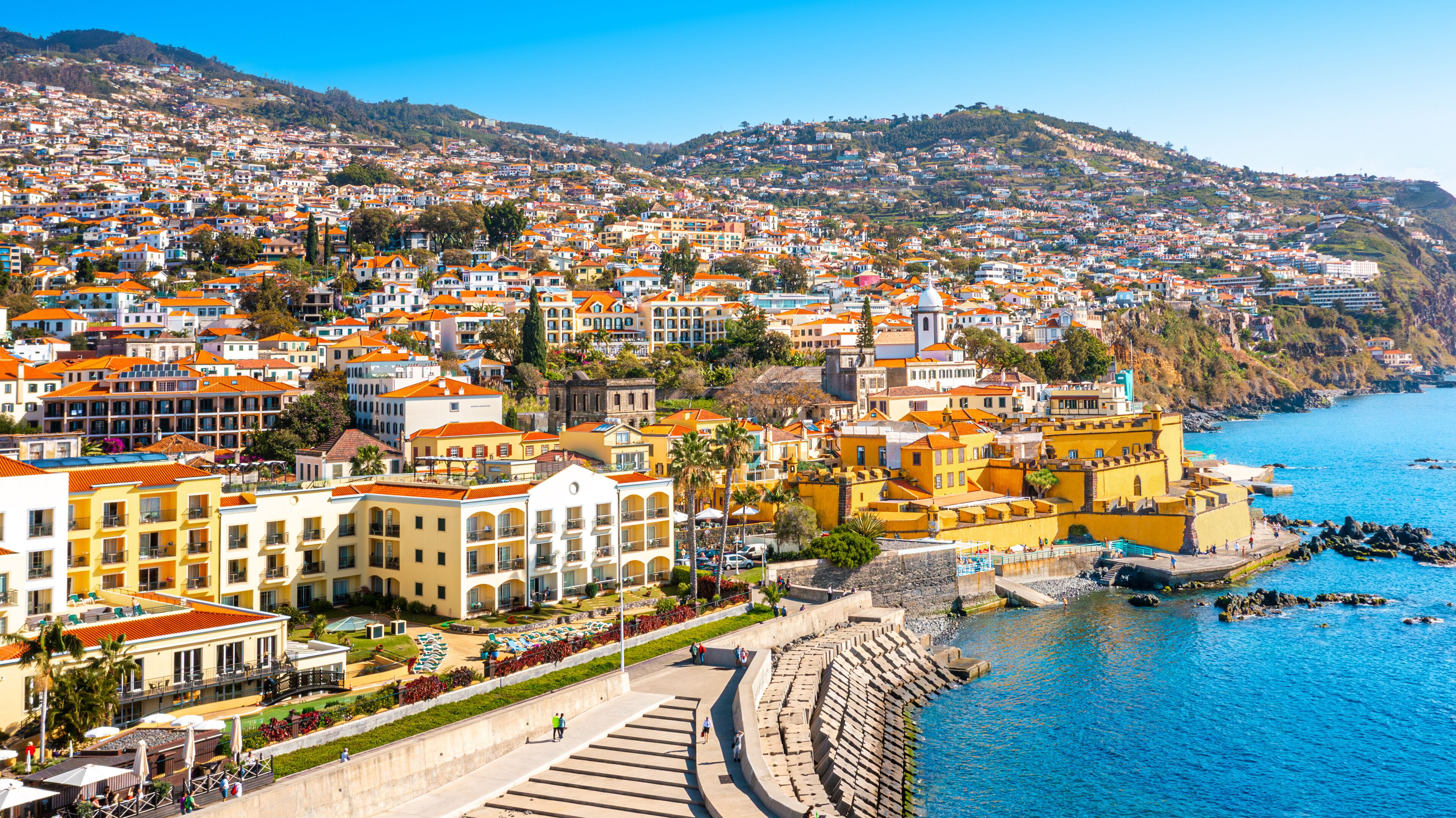 A coastal town with terraced houses, a waterfront promenade, and a historic stone wall.