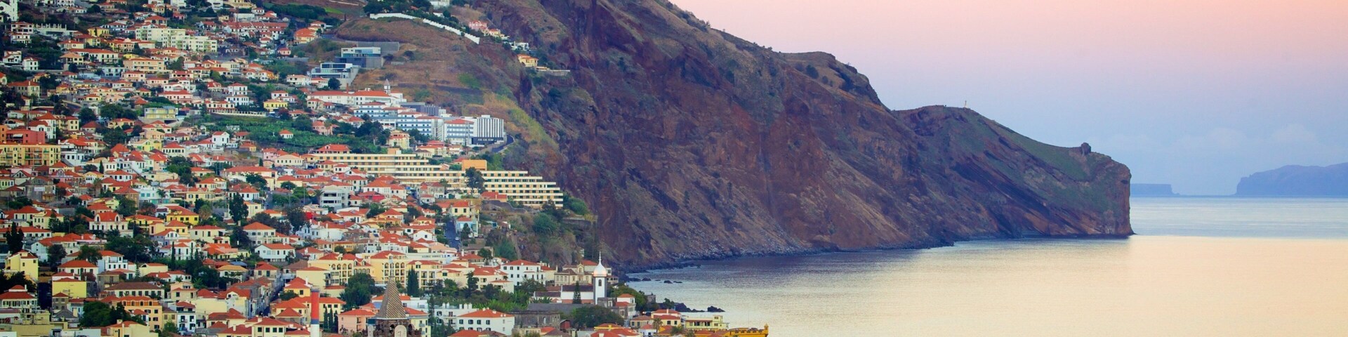 Un pueblo costero con edificios de colores, una ladera pronunciada y mar tranquilo.