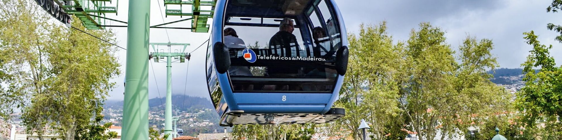 Um teleférico suspenso sobre um parque com edifícios e árvores lá embaixo.