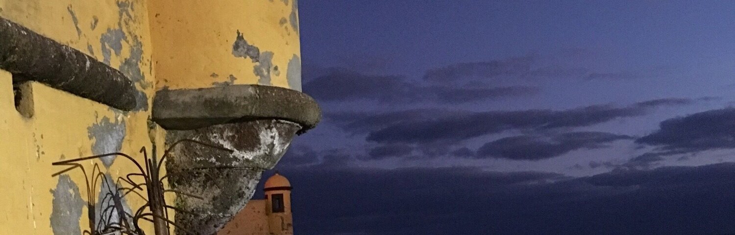 Un edificio costero con fachada amarilla y una pequeña torre, con vista al mar.