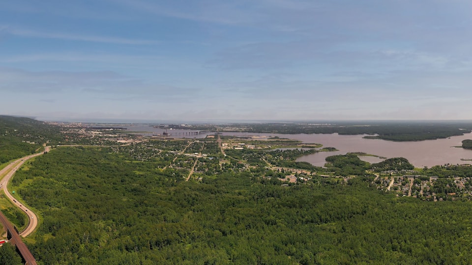 A highway curving through a forested area with a large body of water and a bridge in the distance.