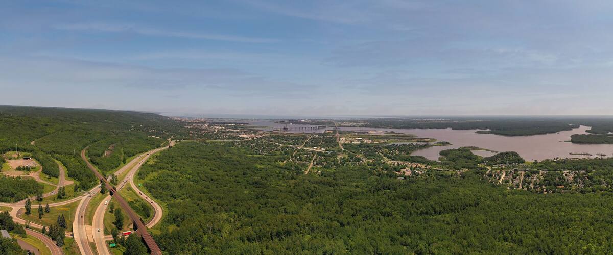 A highway curving through a forested area with a large body of water and a bridge in the distance.