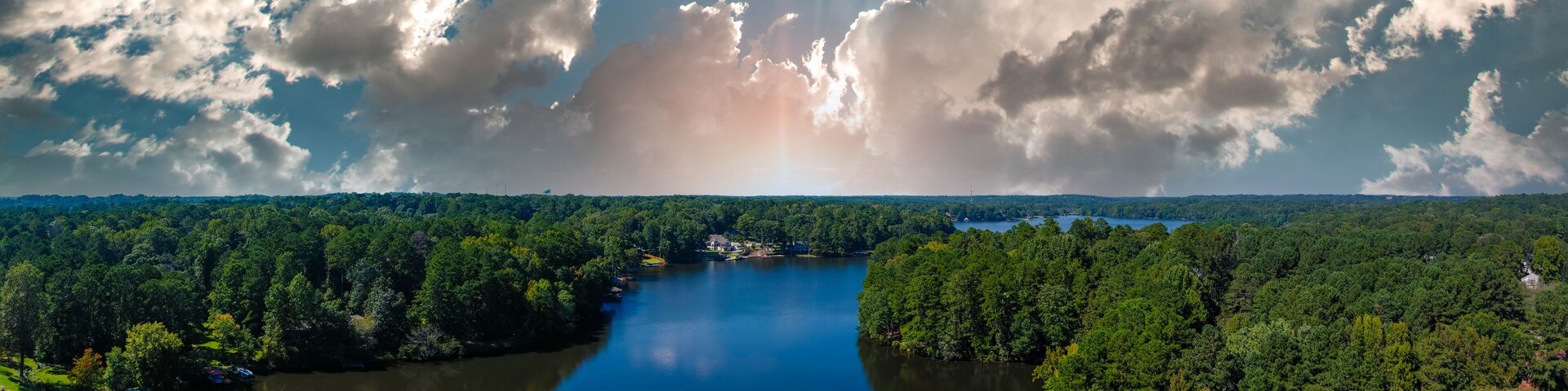 a stunning aerial panoramic shot of the blue waters of Lake Peachtree with vast miles of lush green trees and boats docked along the lake with powerful clouds in Peachtree City Georgia