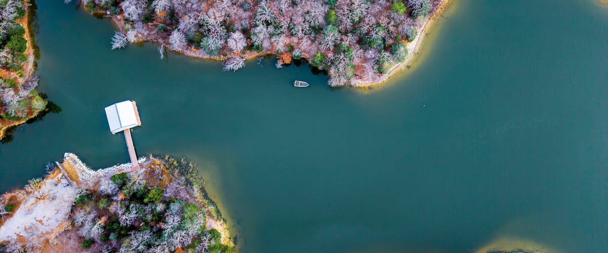 An aerial view of a lake surrounded by forested areas with a dock and a small boat.