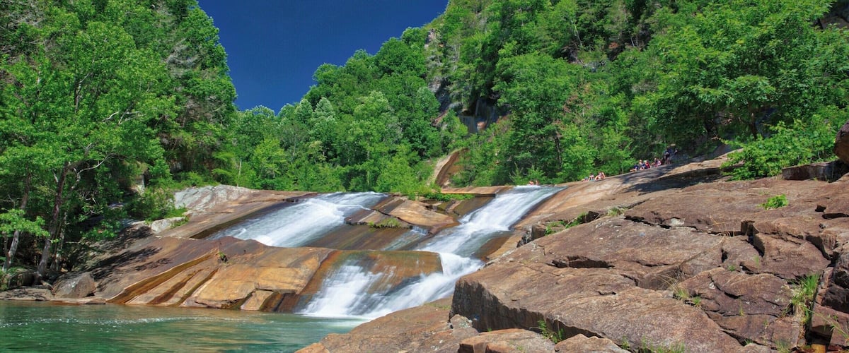 A waterfall cascading over rocky terrain surrounded by dense green foliage.