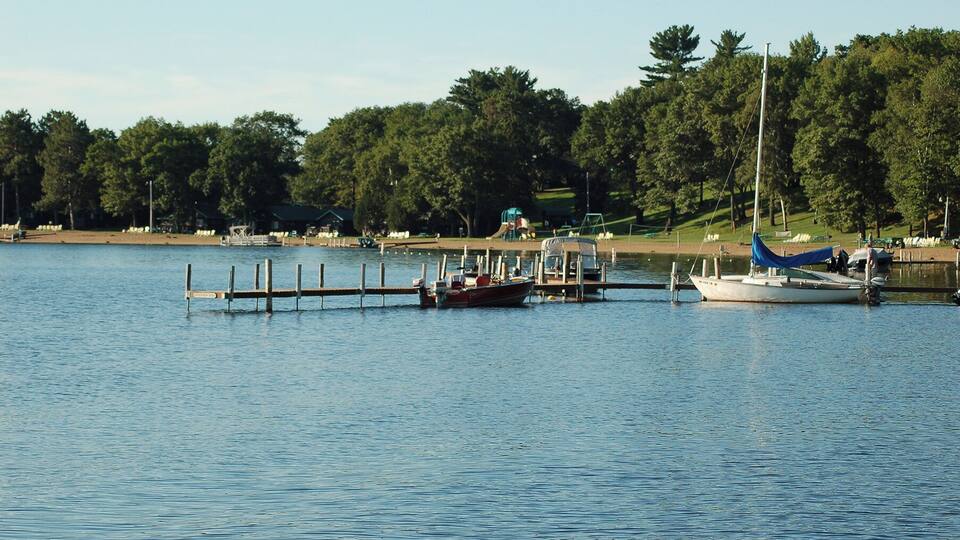 A calm lake with a dock, a small boat, and a sailboat.