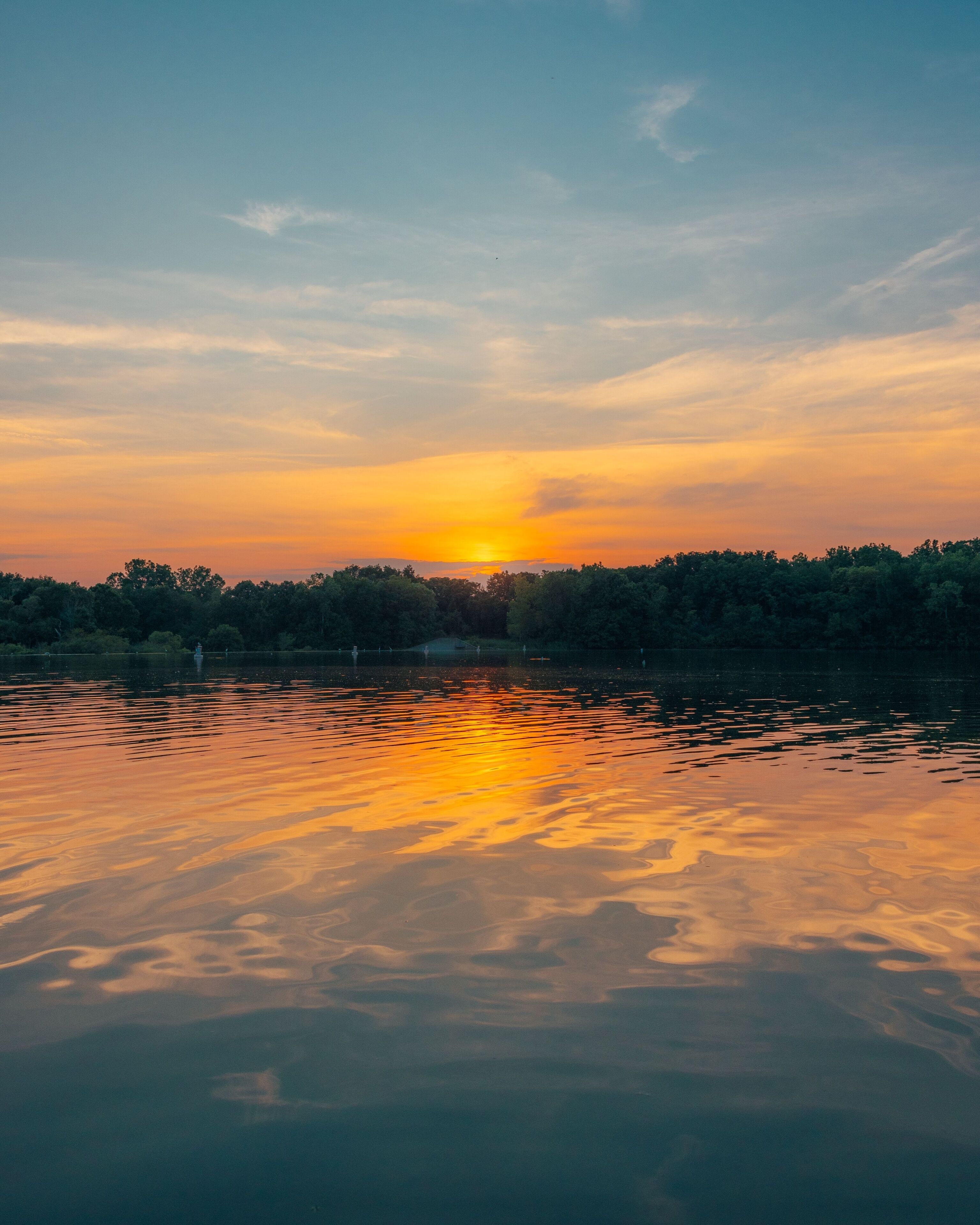 A sunset over a calm lake with reflections of the sky, surrounded by a dense forest.