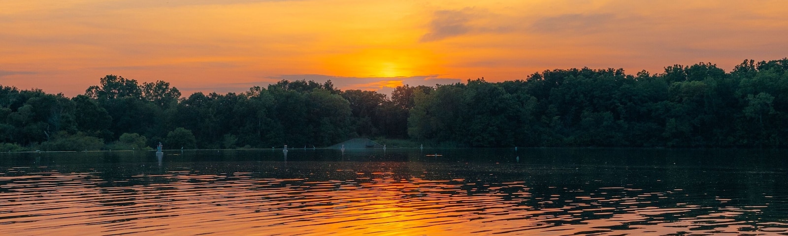 A sunset over a calm lake with reflections of the sky, surrounded by a dense forest.