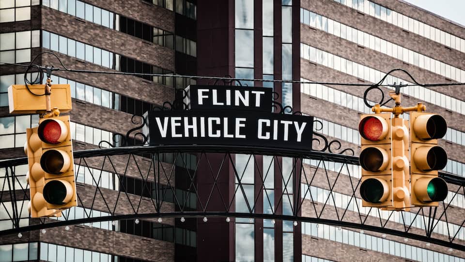 A traffic light and a sign that reads 'FLINT VEHICLE CITY' above a building with a grid of windows.