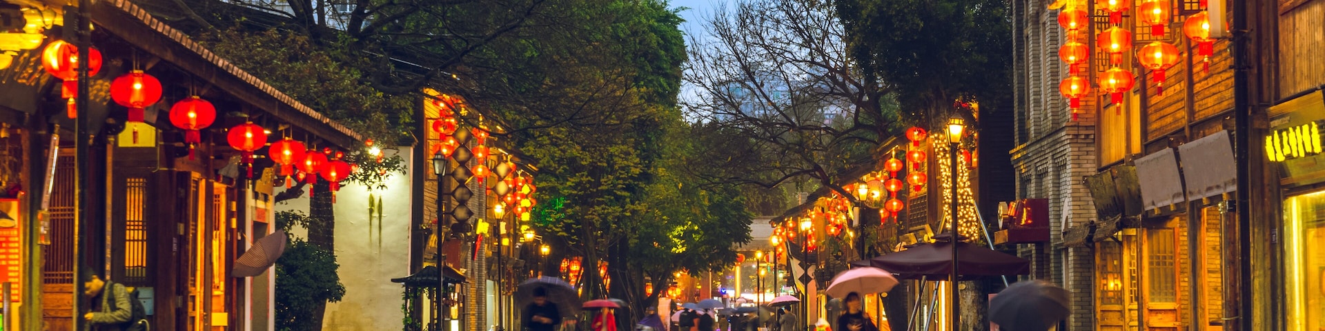 Rua molhada com edifícios tradicionais e lanternas vermelhas.