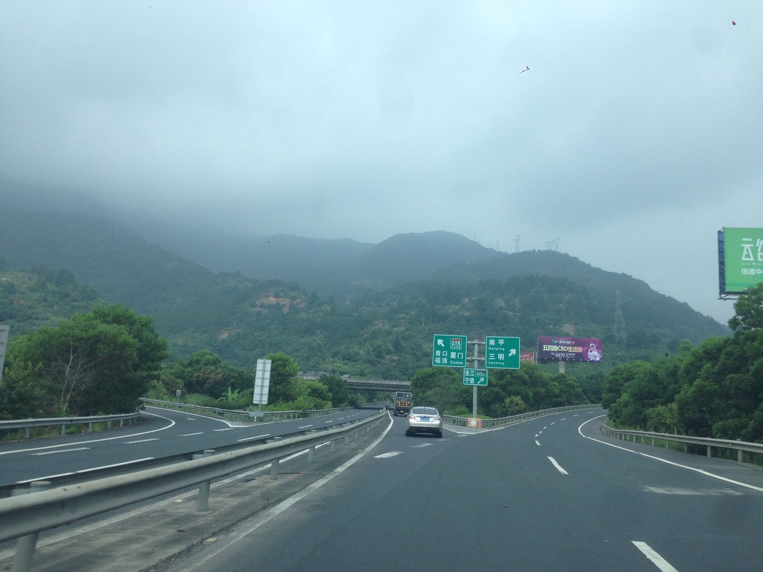 A highway with multiple lanes, green directional signs, and a mountainous landscape in the background.